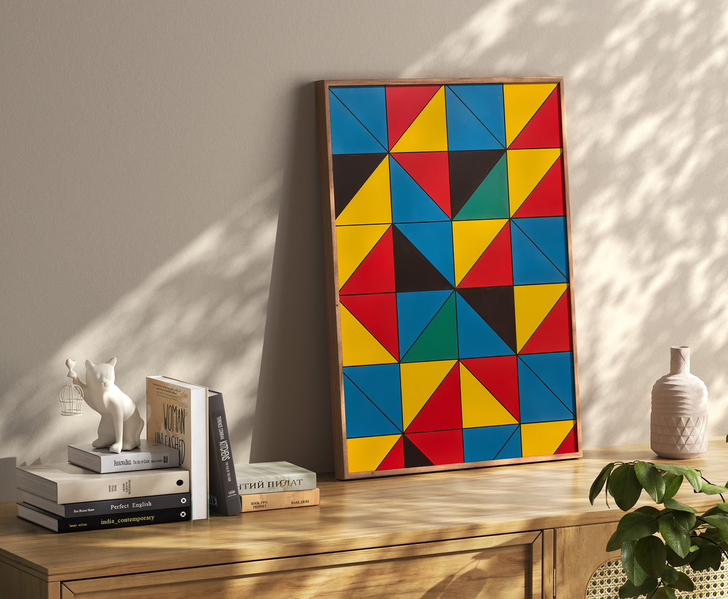 Colorful geometric abstract painting leaning on a wall beside books and a small plant.