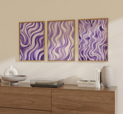Three framed abstract purple wavy artworks on a wall above a wooden sideboard with decorative items.