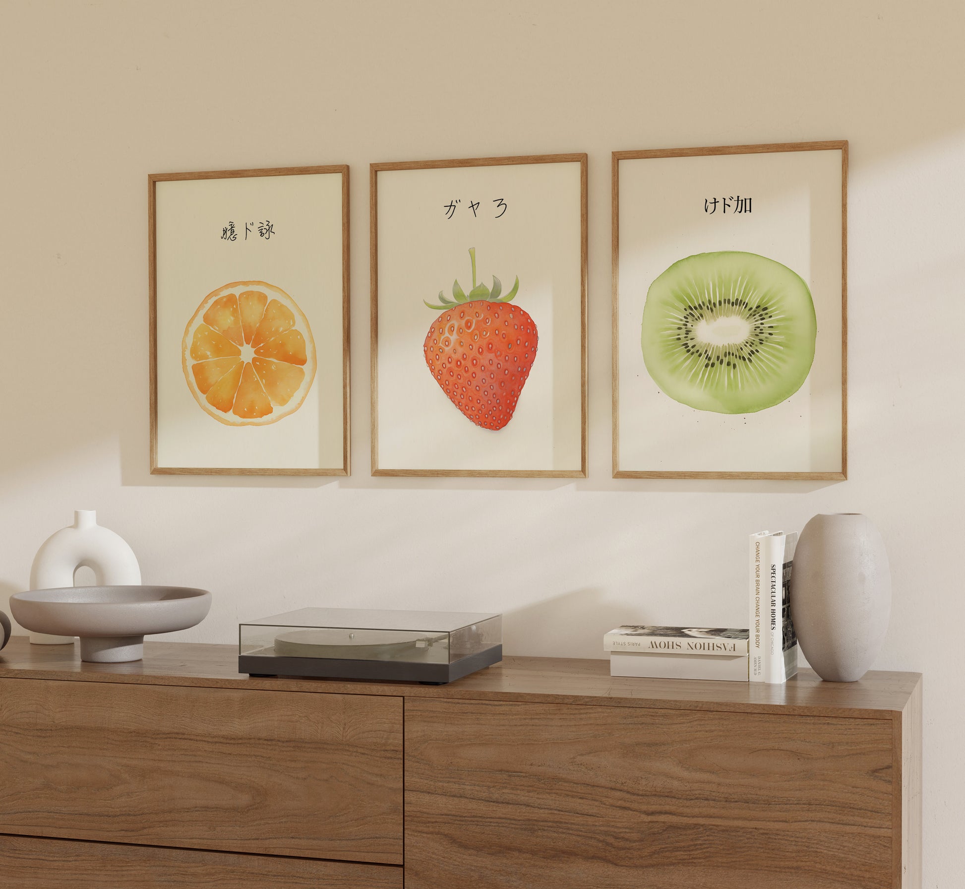 Three framed pictures of fruit with Japanese writing hanging on a wall above a sideboard.