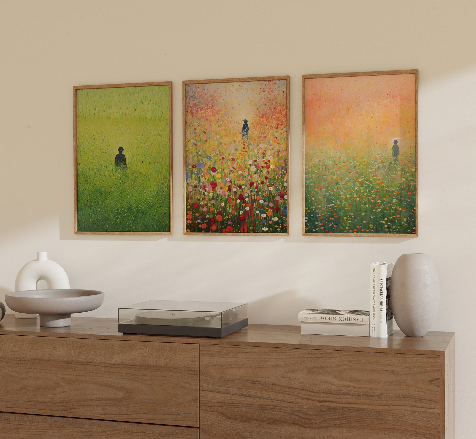 Three framed paintings of solitary figures in fields on a wall above a wooden sideboard with decorative items.