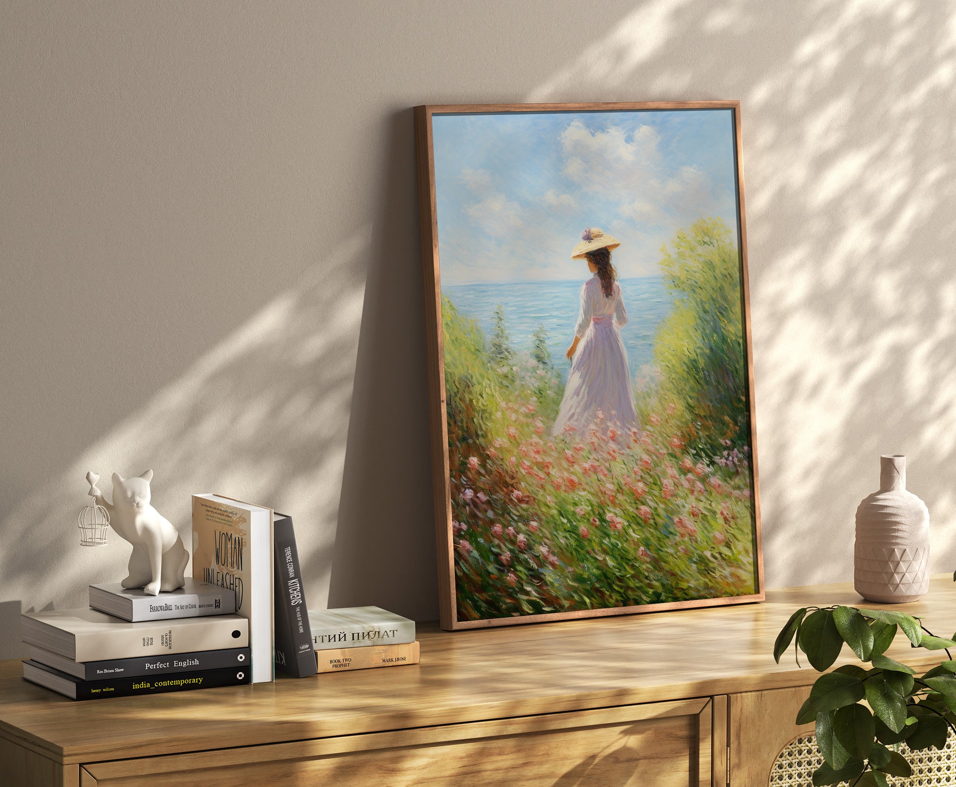 Painting of a woman in a field by the sea, on a console with decor and books.