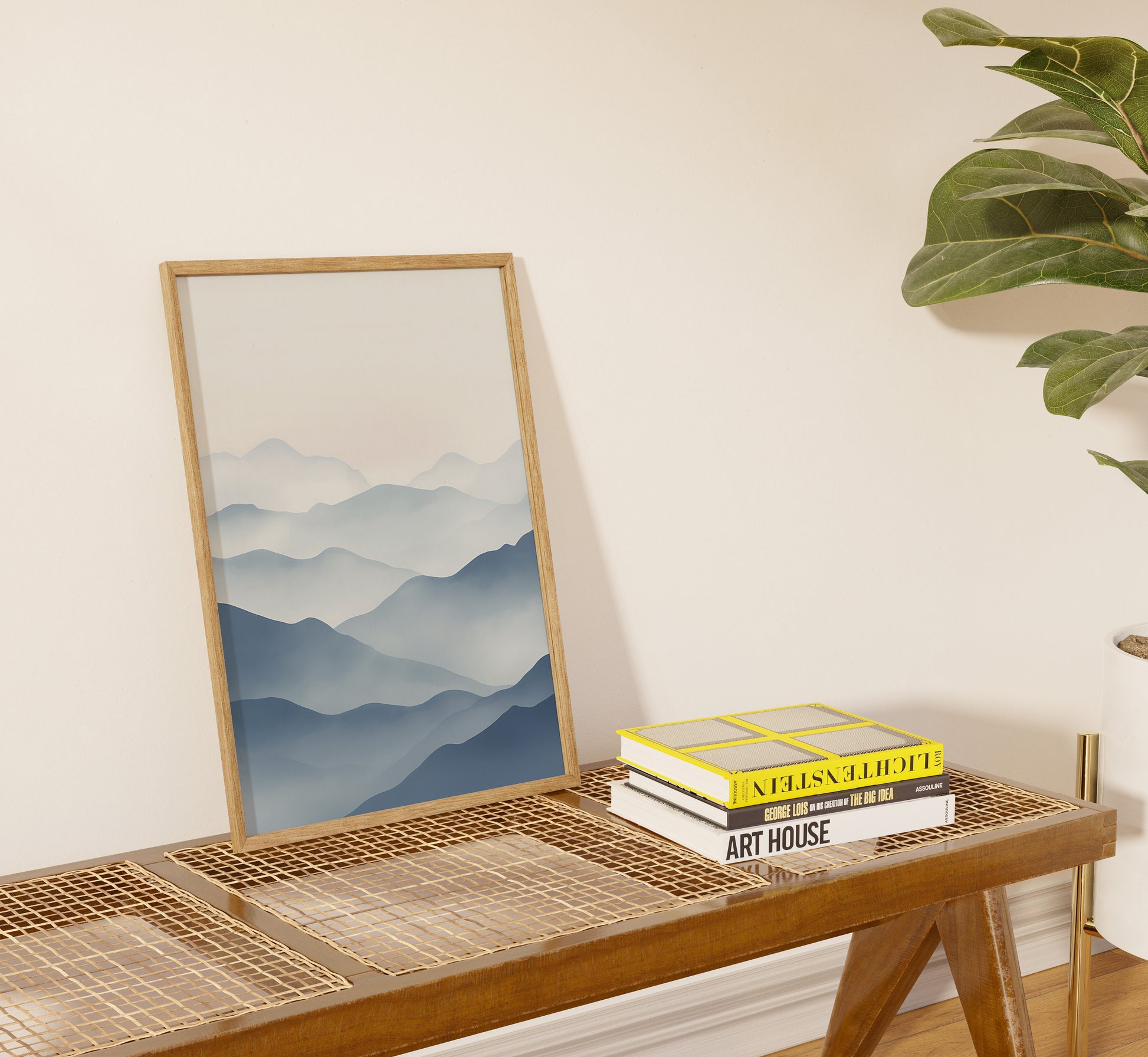 Framed painting of mountains on console table beside books.
