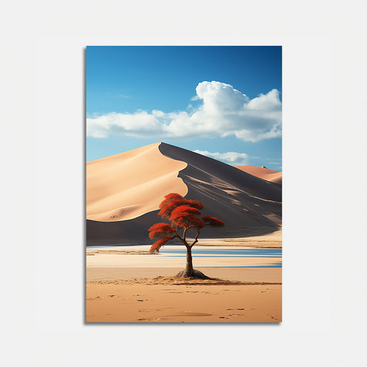 A solitary tree with red leaves stands in front of a large sand dune under a blue sky with clouds.