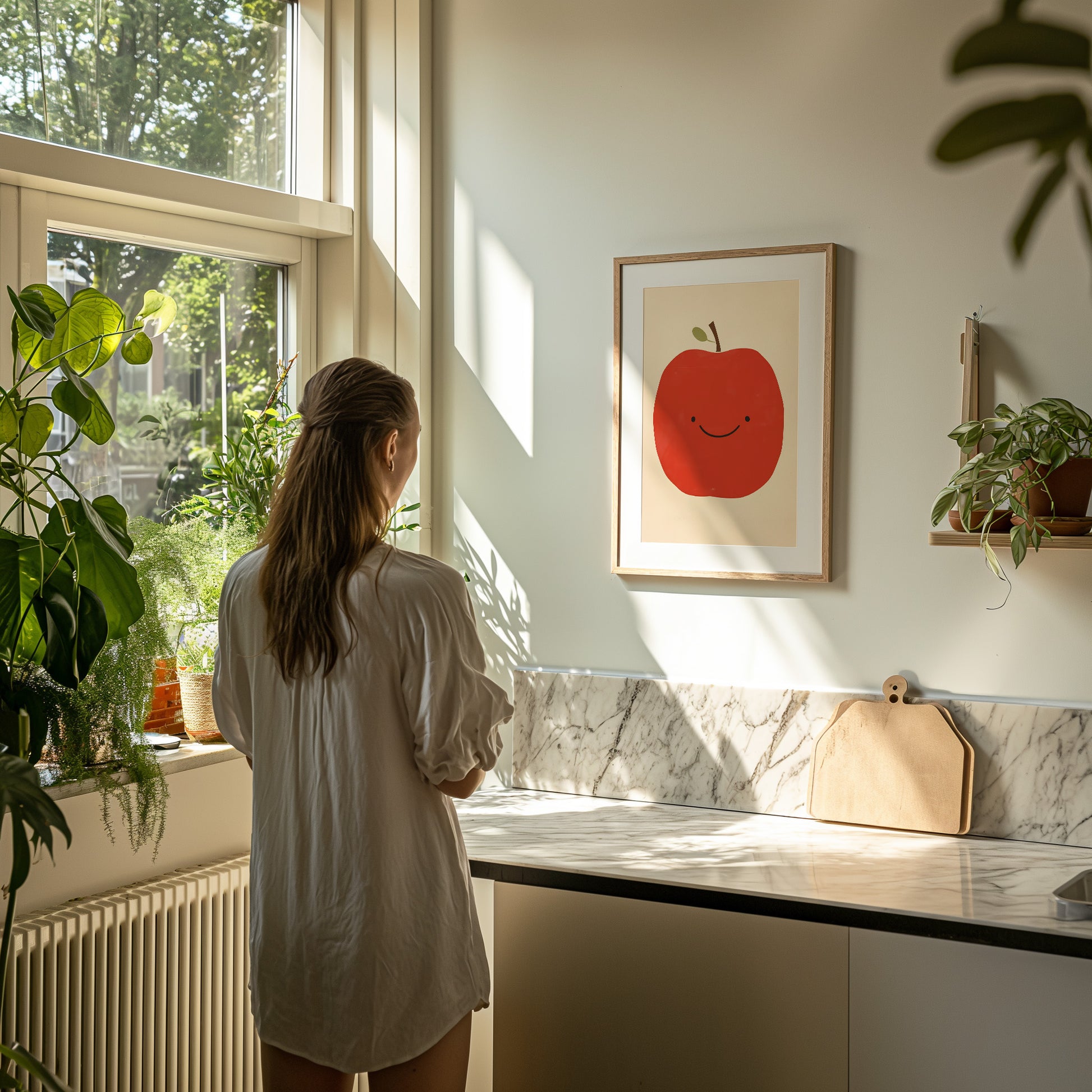 A person standing by a window looking at a framed apple picture in a sunny room.