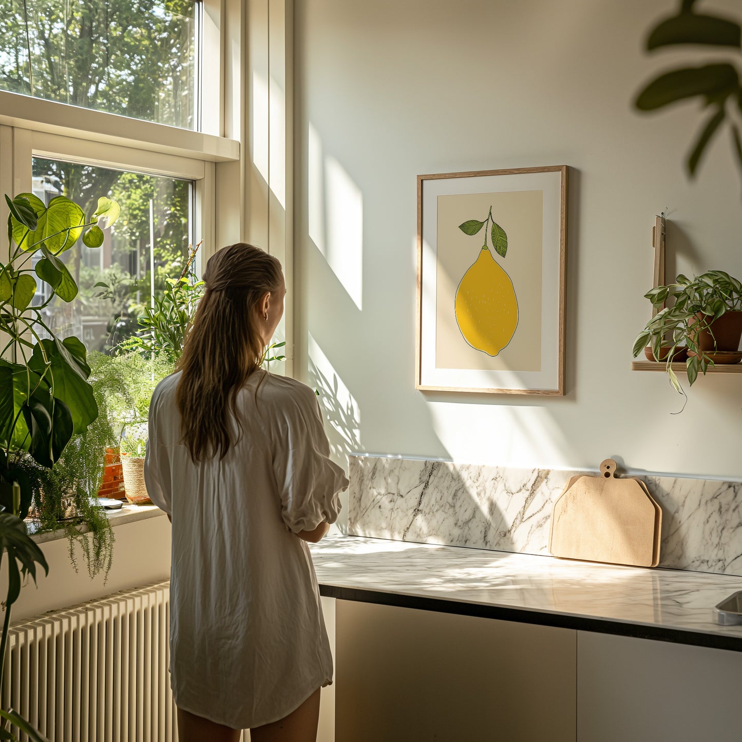 A person in a white shirt looking out a sunlit window in a room with plants and a lemon artwork.