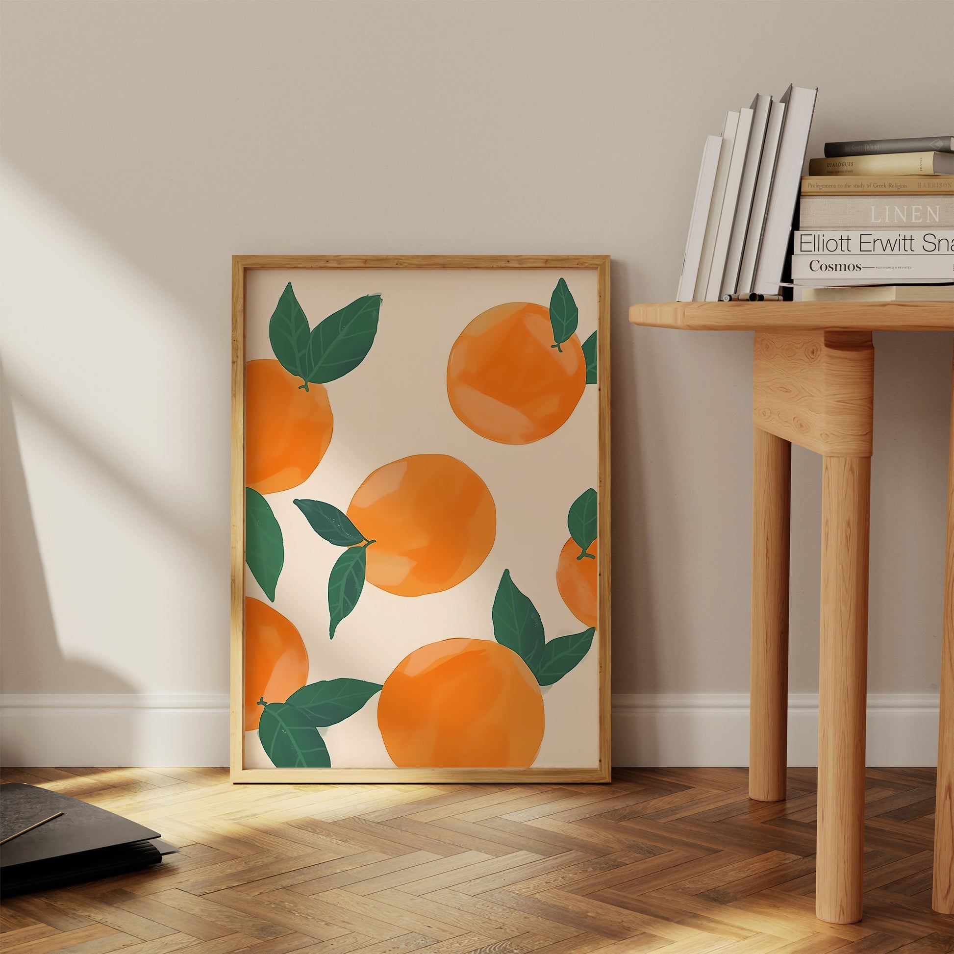 A framed artwork of oranges with leaves leaning against a wall beside a wooden table.