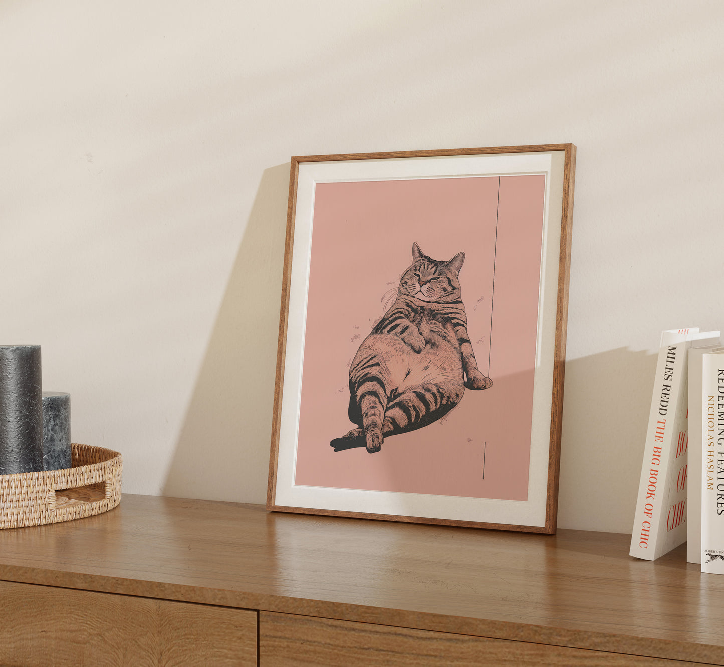 Framed illustration of a cat lying on its back displayed on a shelf.