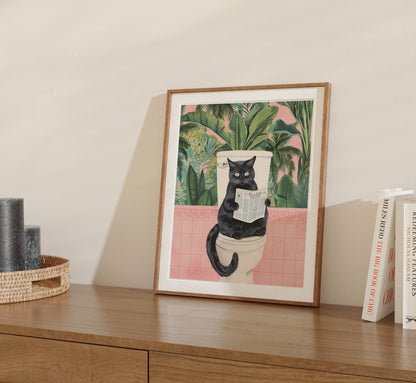 A framed illustration of a black cat reading a newspaper on a wooden sideboard.