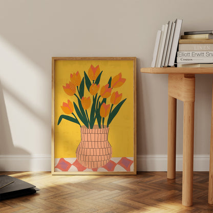 A framed poster with a tulip bouquet illustration leaning against a wall beside a wooden table.