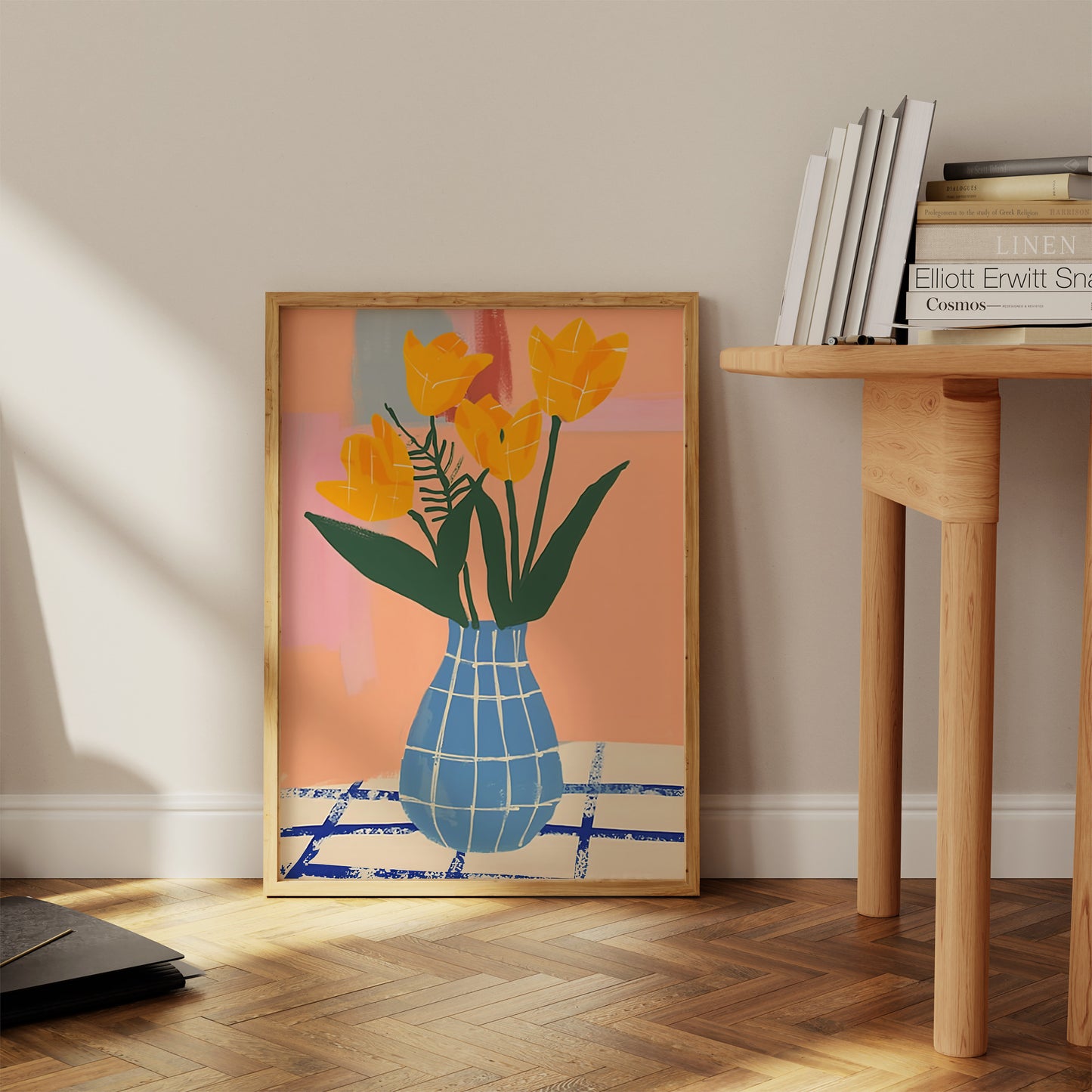 A framed poster of yellow tulips in a blue vase, next to books on a wooden floor.