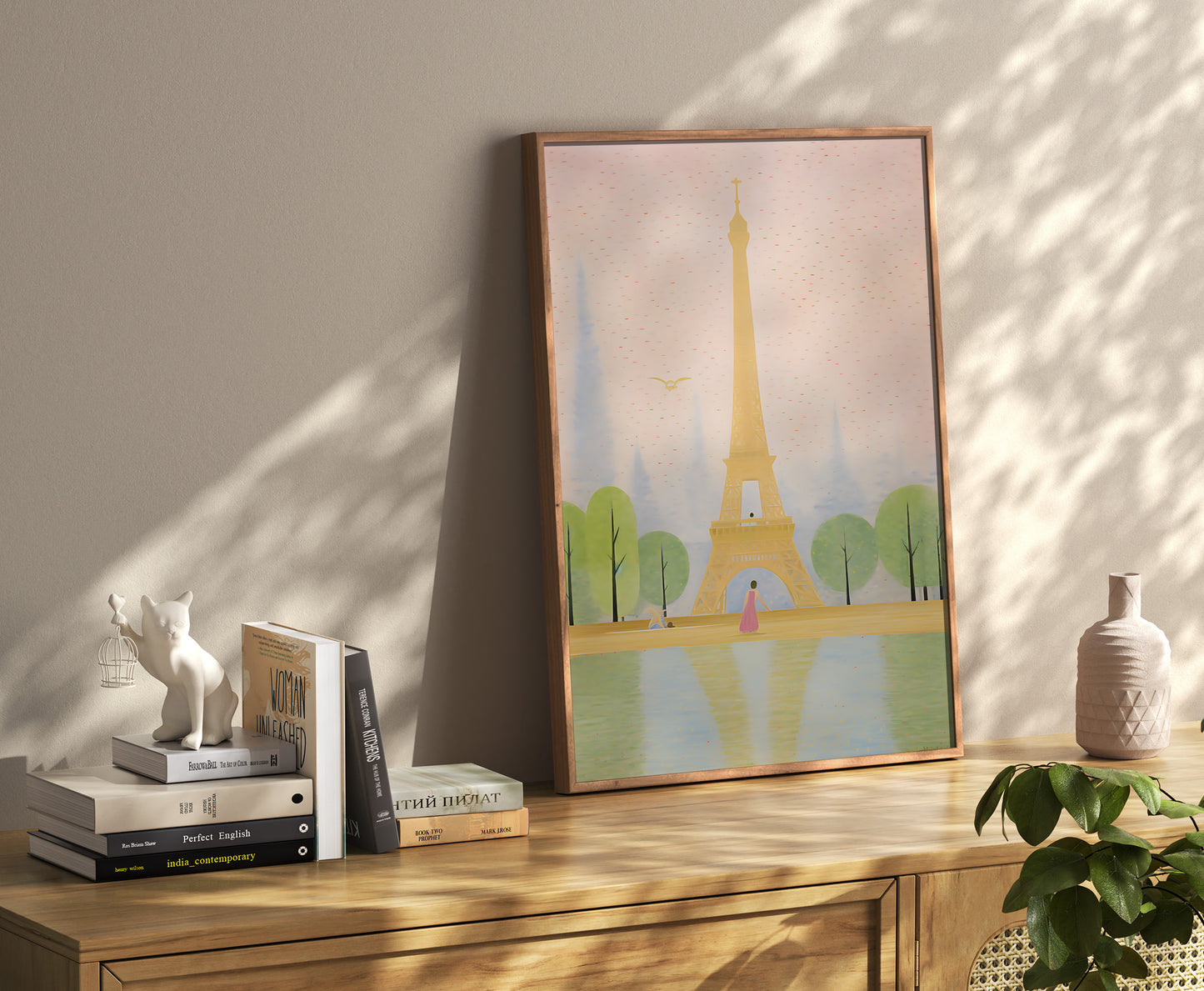A framed illustration of the Eiffel Tower on a console table with books and decorative objects.