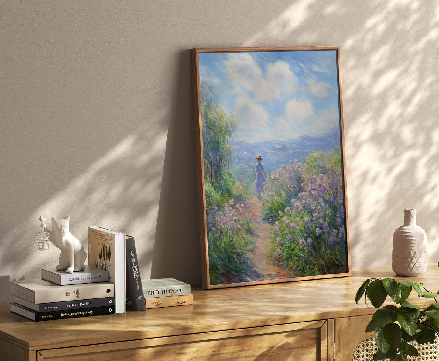 A framed impressionist painting of a figure on a path beside books and decor on a credenza.