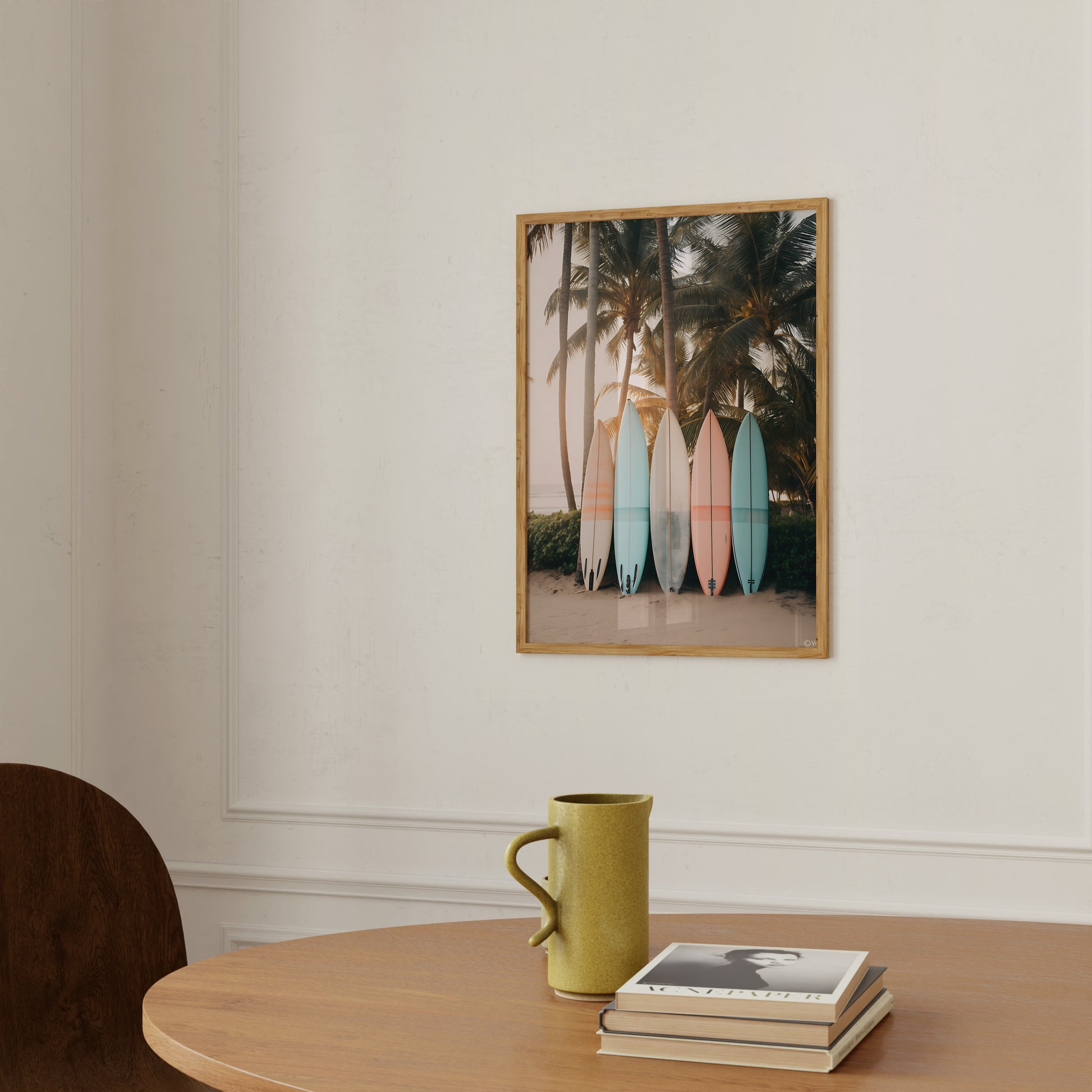 A picture of surfboards against palm trees on a wall above a table with a mug and books.