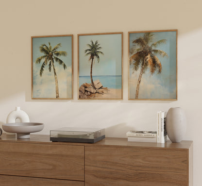 Three framed tropical beach paintings over a wooden sideboard.