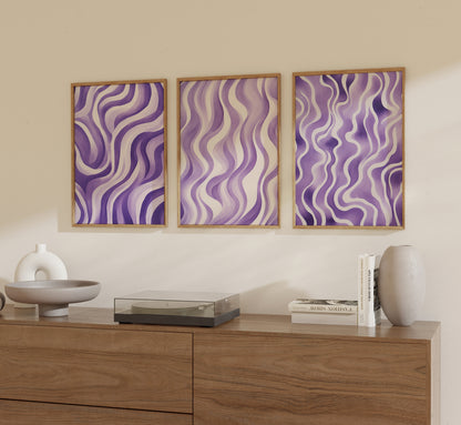 Three framed abstract purple wavy patterns on a wall above a wooden sideboard.