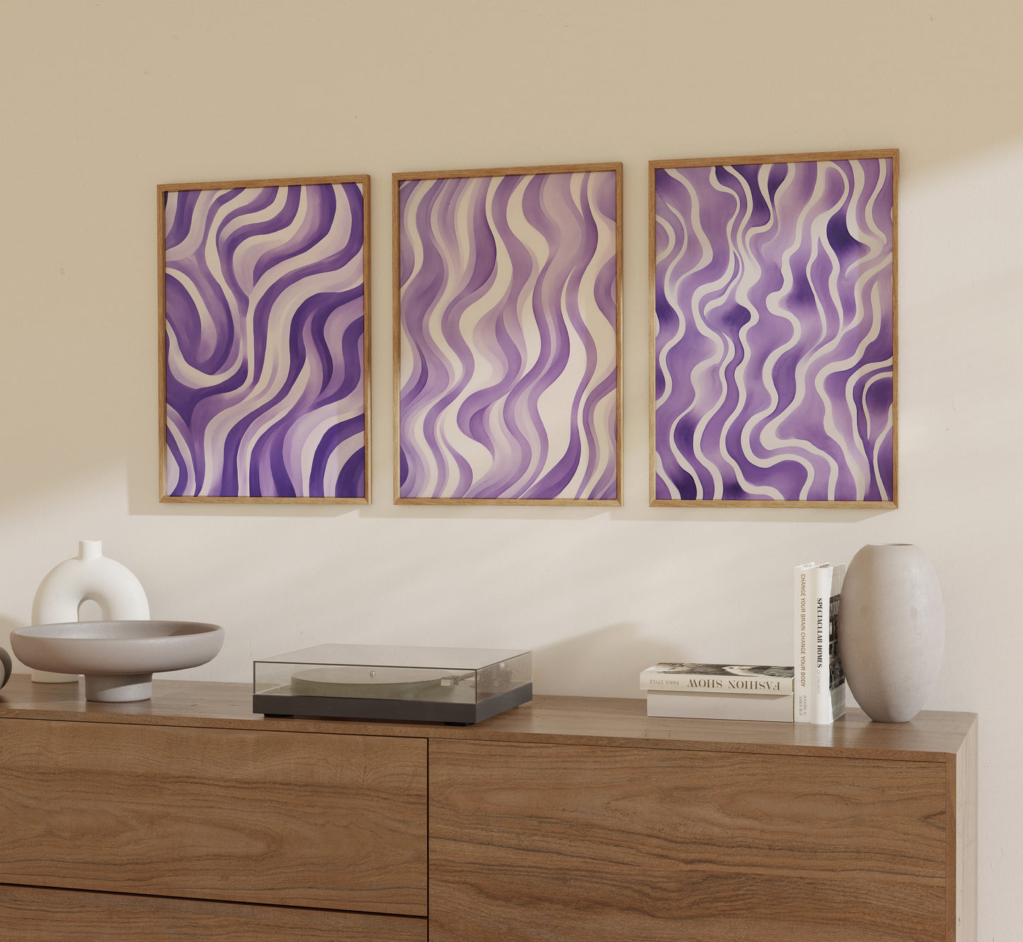 Three framed abstract purple wave pattern artworks hanging on a wall above a wooden sideboard with decorative items.