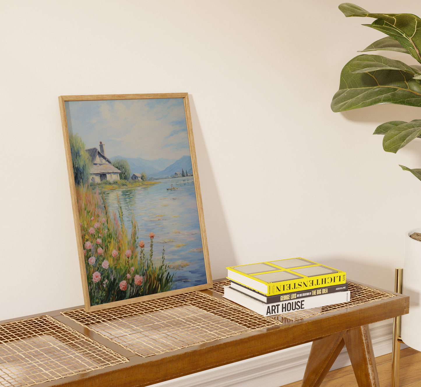 A framed landscape painting leaning against a wall above a table with books.