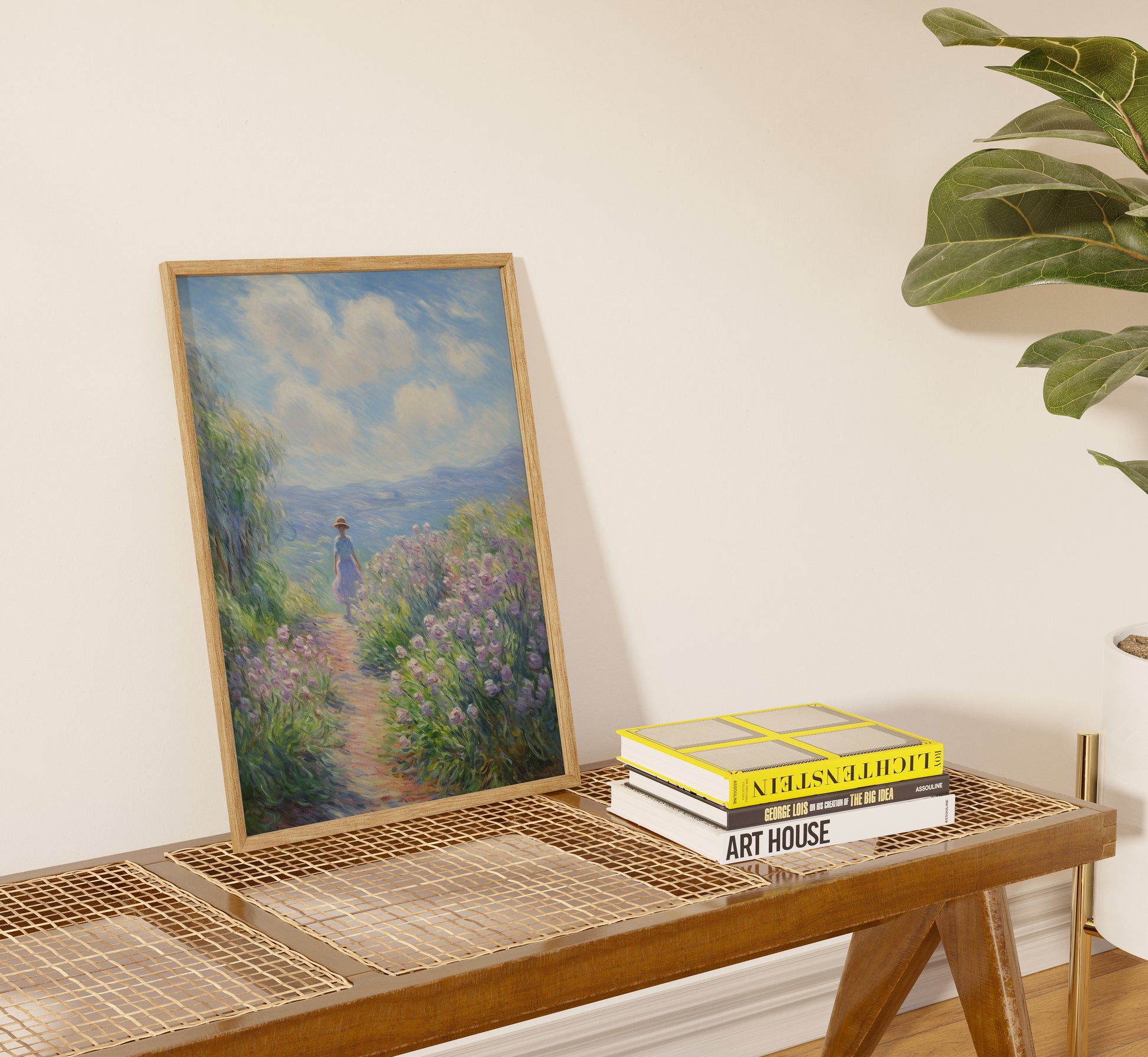 A framed painting of a garden path with books on a table beside it.