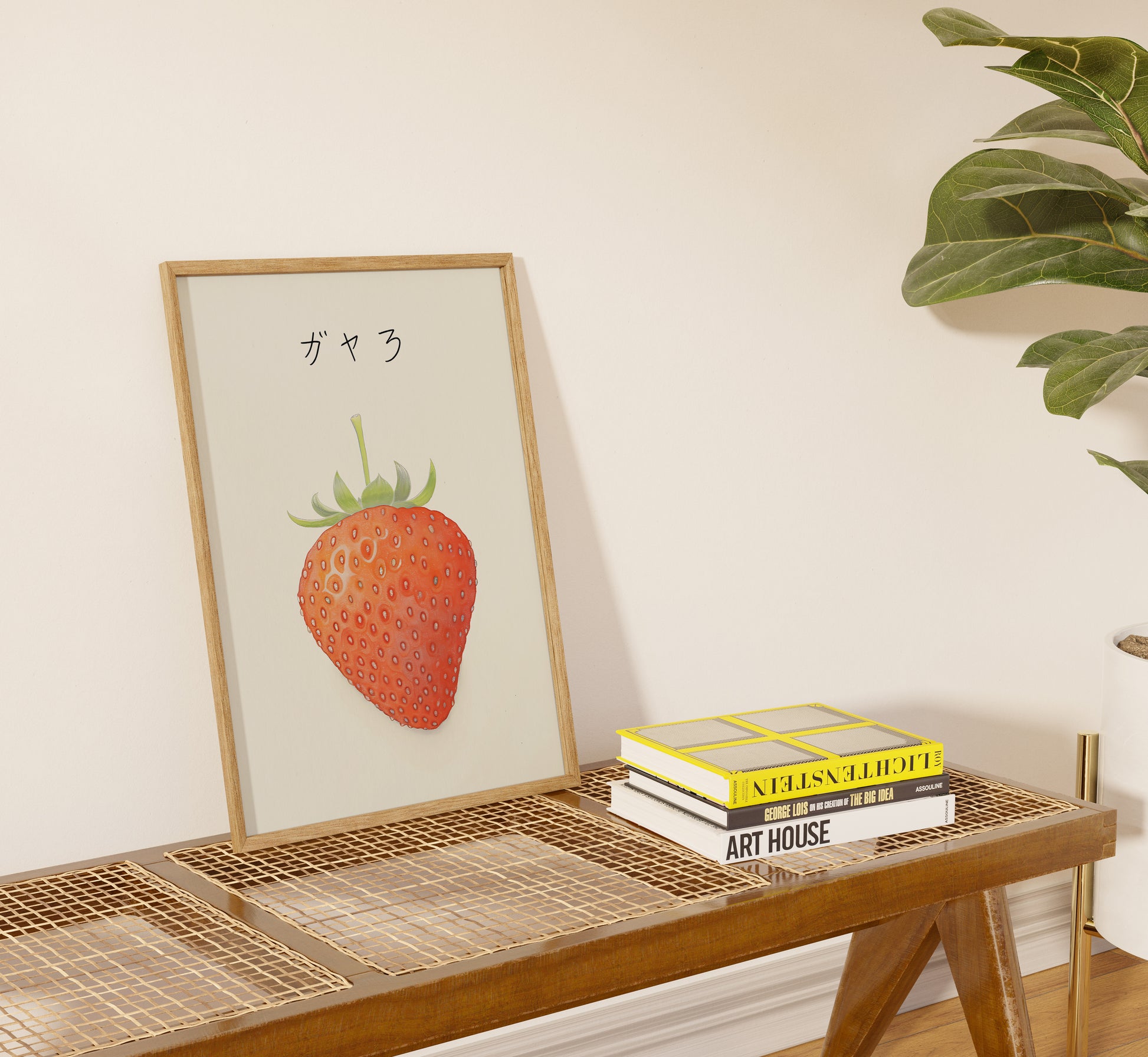 Framed artwork of a strawberry with Japanese text above, on a table beside books.