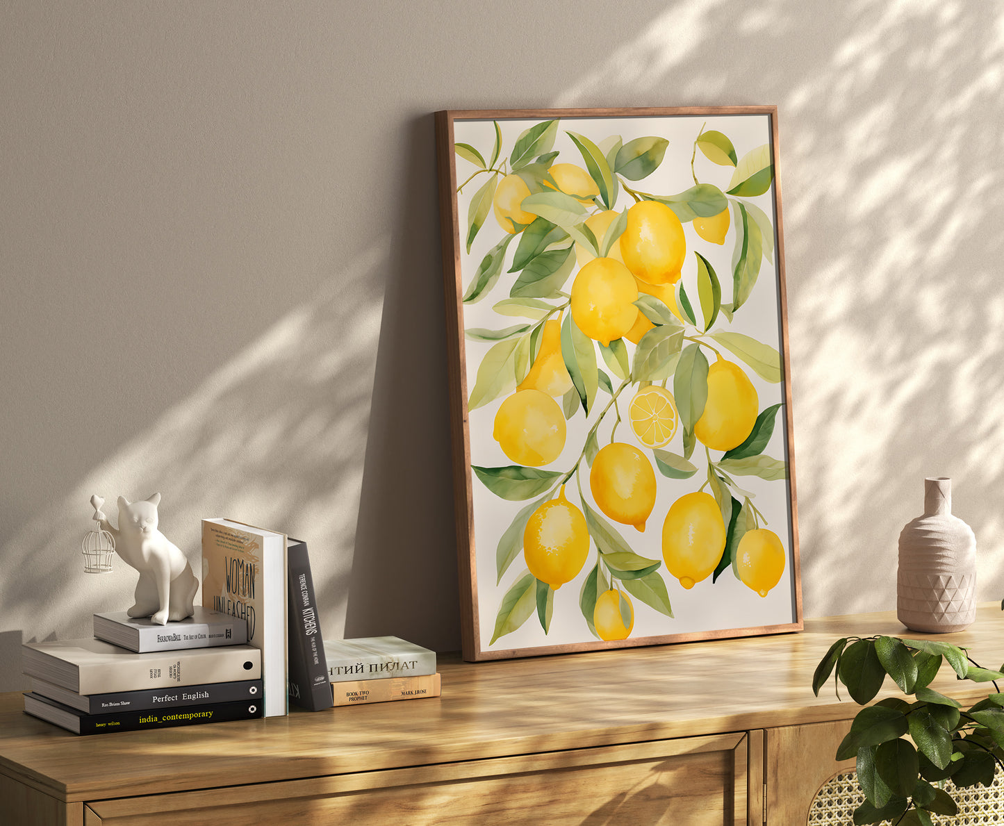 A framed painting of lemons on a wall above a sideboard decorated with books and vases.