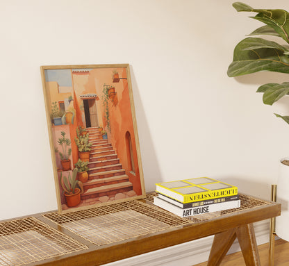 A framed painting of a stairway placed against a wall beside books on a table.