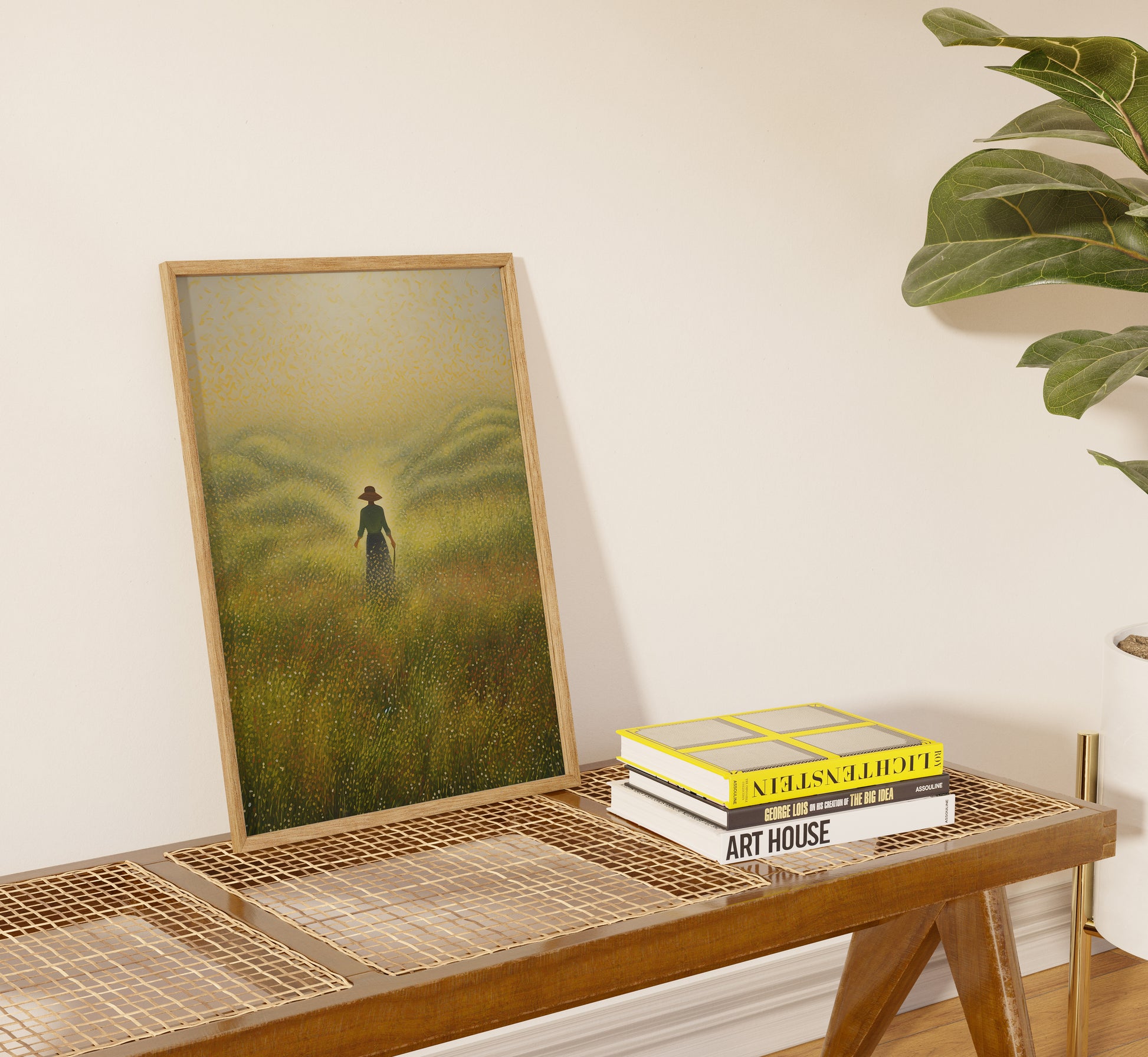 A framed painting of a figure in a field next to books on a woven table.