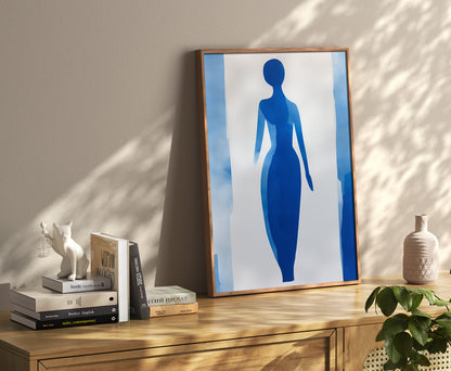 Abstract blue silhouette artwork in a frame on a wooden sideboard with books and decor.