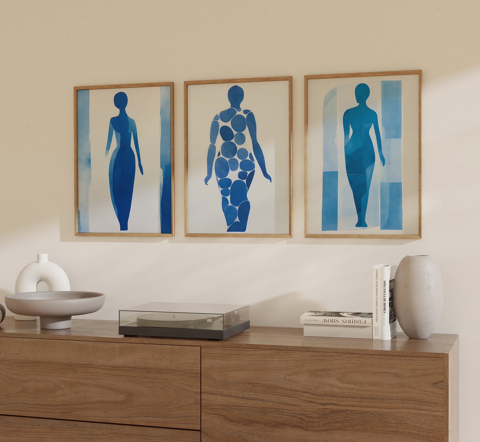 Three abstract framed art pieces depicting blue silhouetted figures on a wall above a wooden sideboard.
