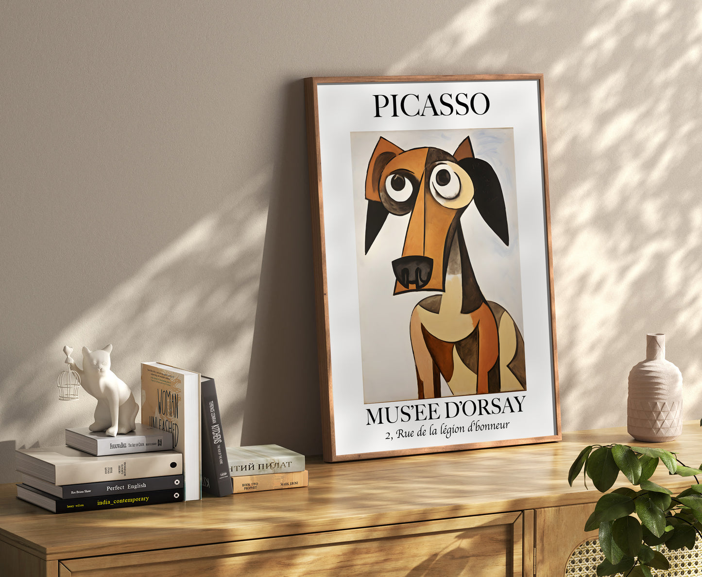 A framed Picasso poster of an abstract dog, on a shelf with decorative items and books.