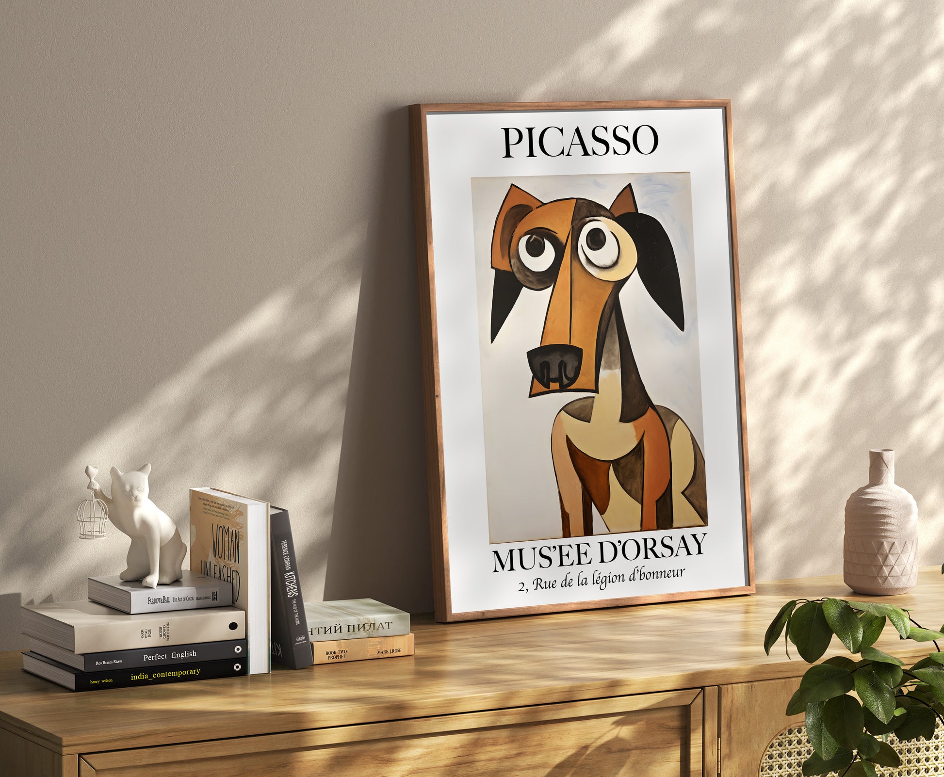 A framed Picasso poster of an abstract dog, on a shelf with decorative items and books.