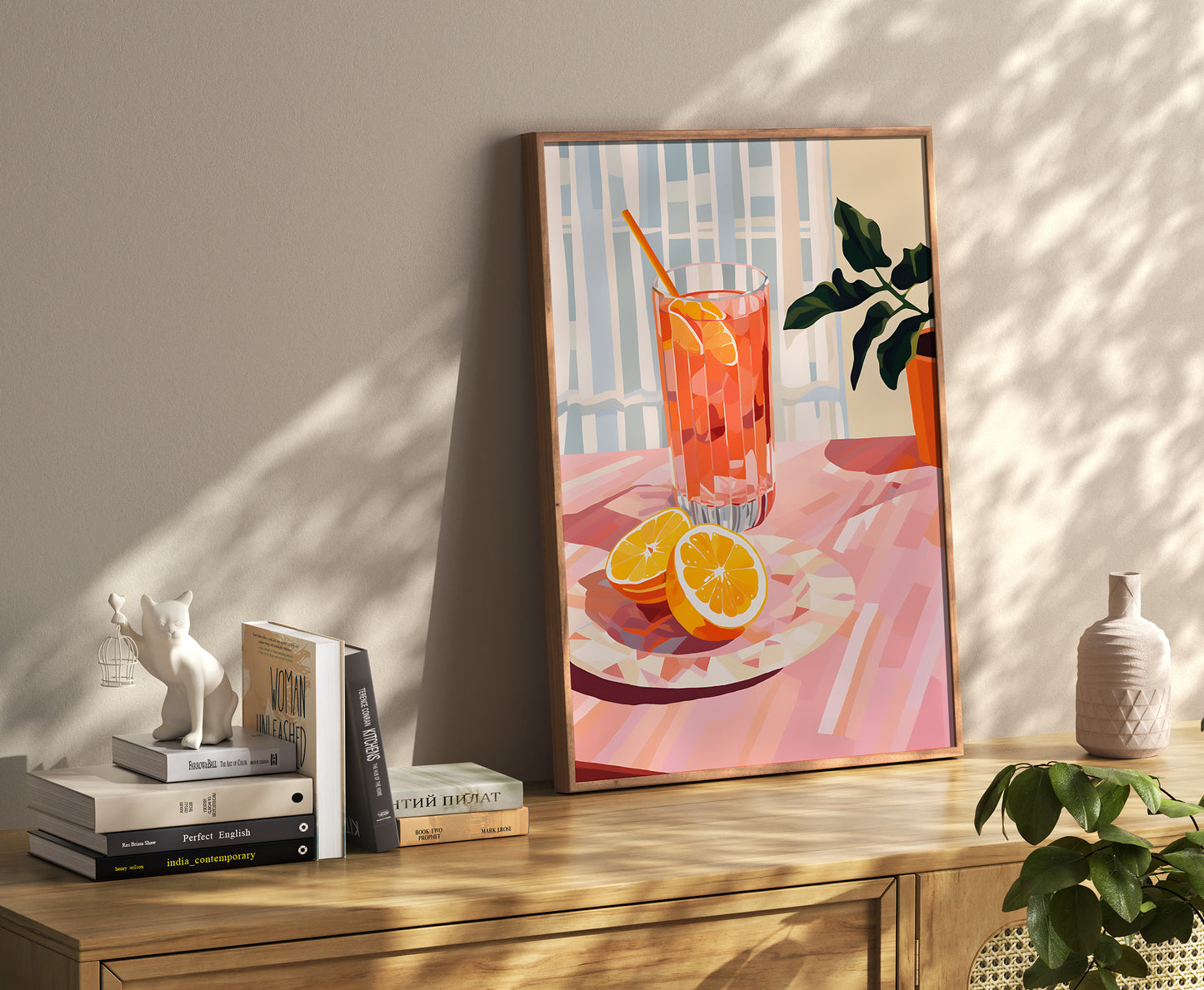 A framed painting of a vibrant orange drink on a sunny table, adorned with decor and books.