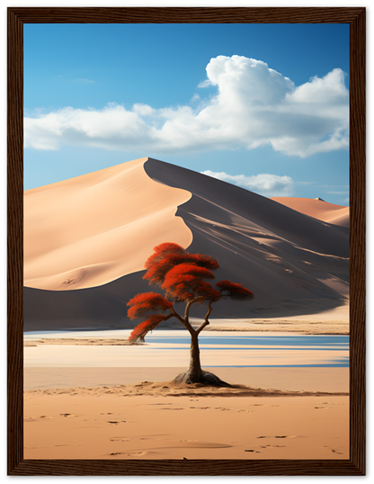 A framed picture of a lone tree with red leaves in a desert with sand dunes and a blue sky.