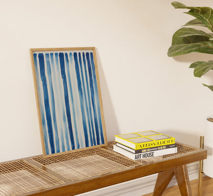 A framed abstract blue artwork leaning against a wall on a console table with books.