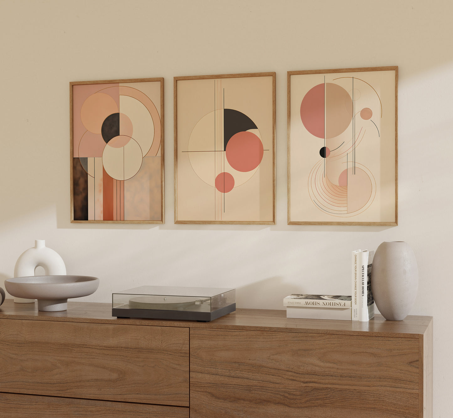 Three abstract art pieces in warm tones hanging on a beige wall above a wooden cabinet.