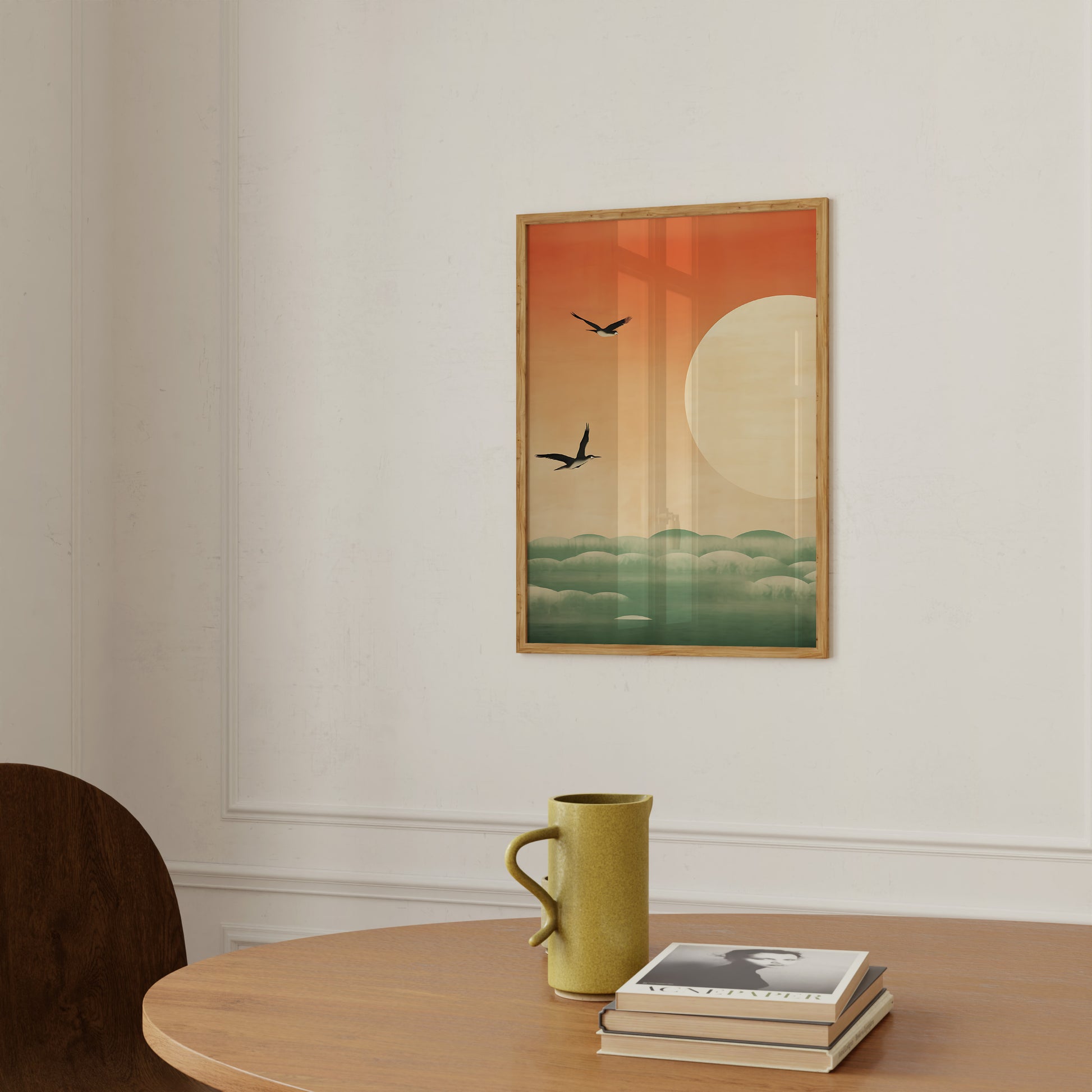 An art print featuring a sun, clouds, and birds on a wall above a table with a mug and books.