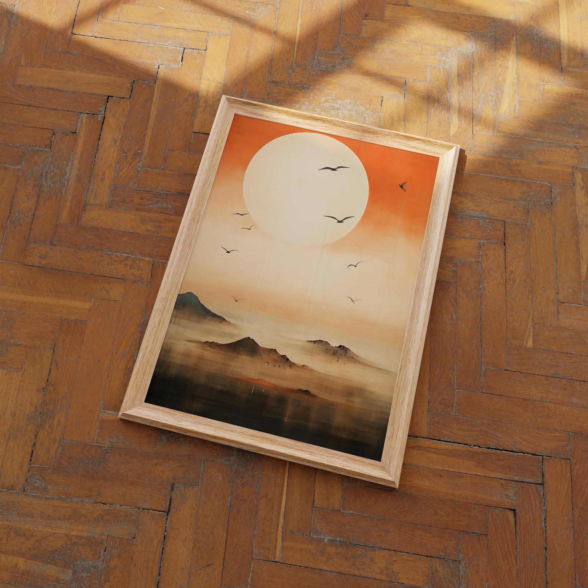 A framed painting of a sunset over mountains with birds in flight, lying on a wood parquet floor.