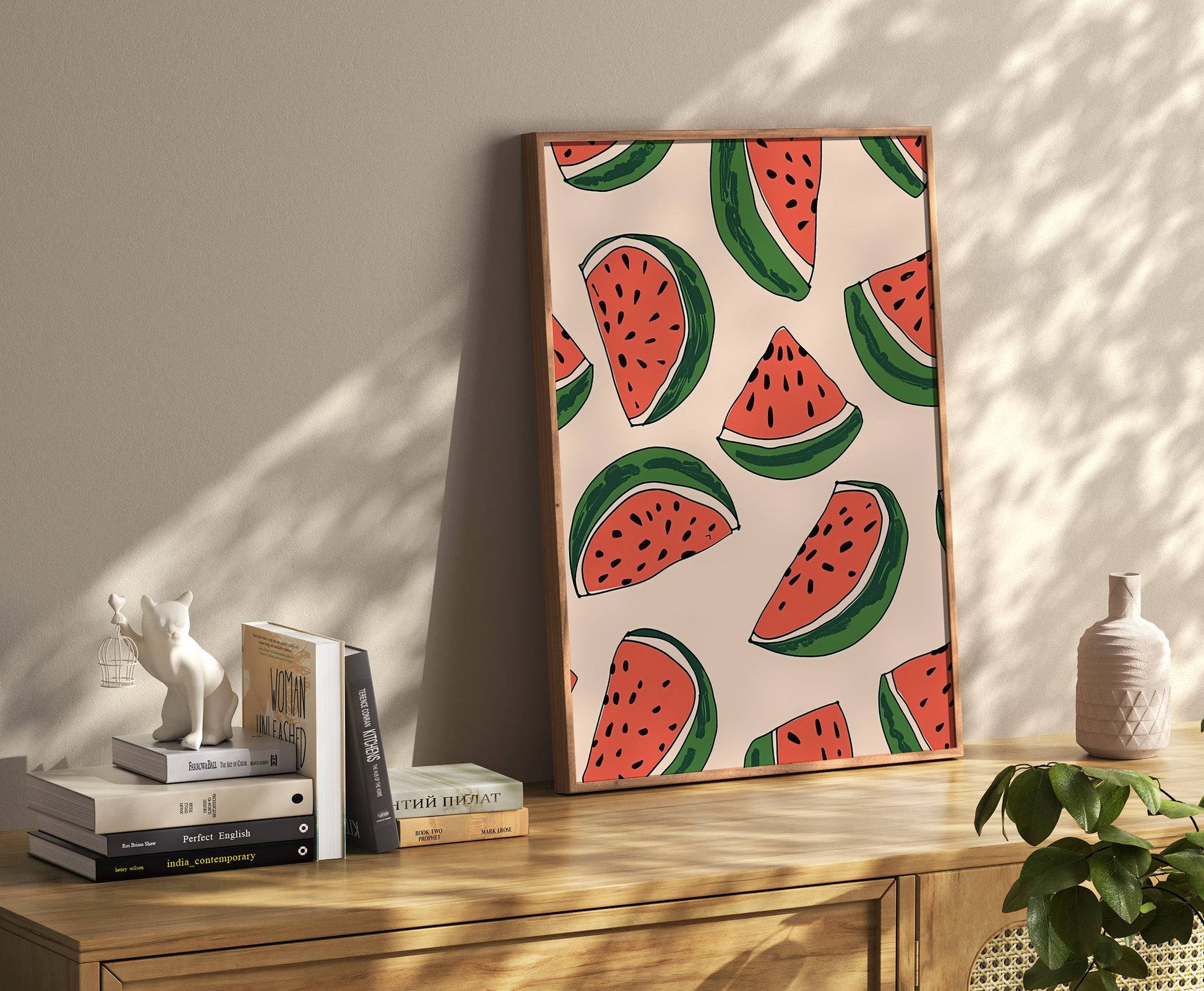 A canvas with a watermelon pattern leaning against a wall on a wooden sideboard with books and decorations.