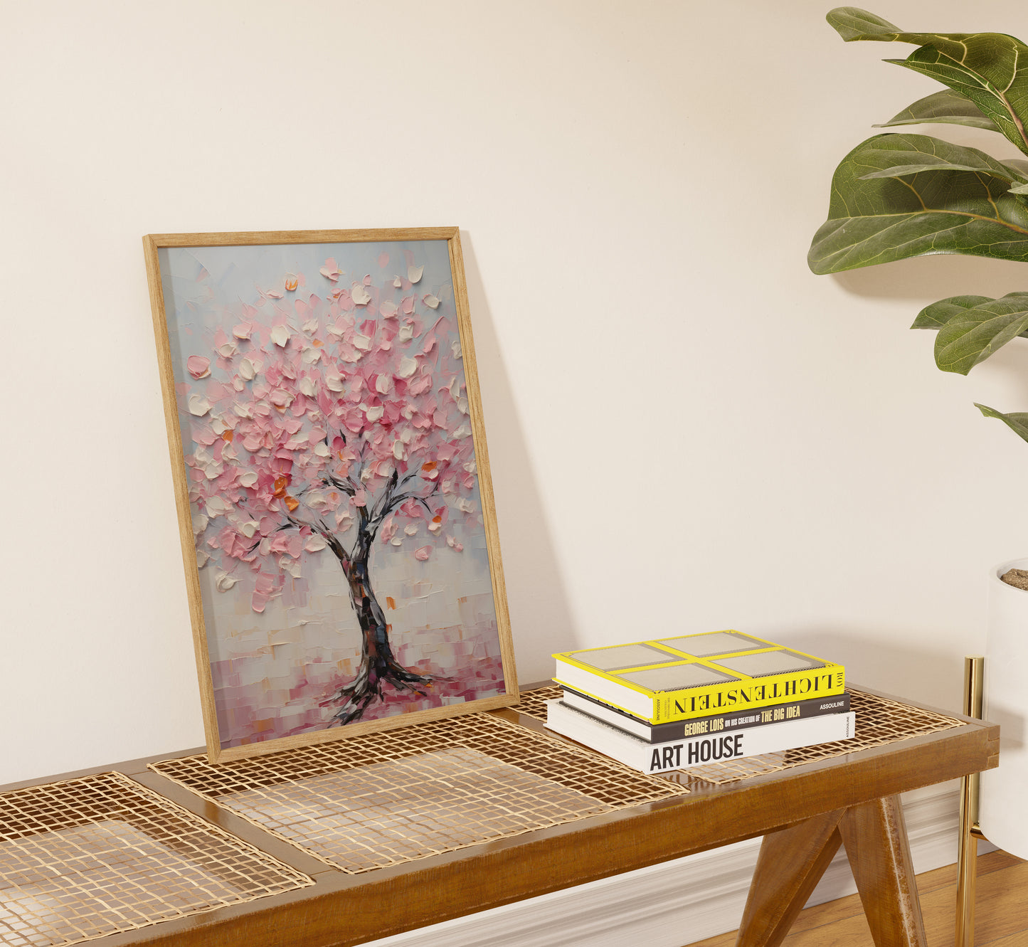 A framed painting of a cherry blossom tree beside books on a console table.