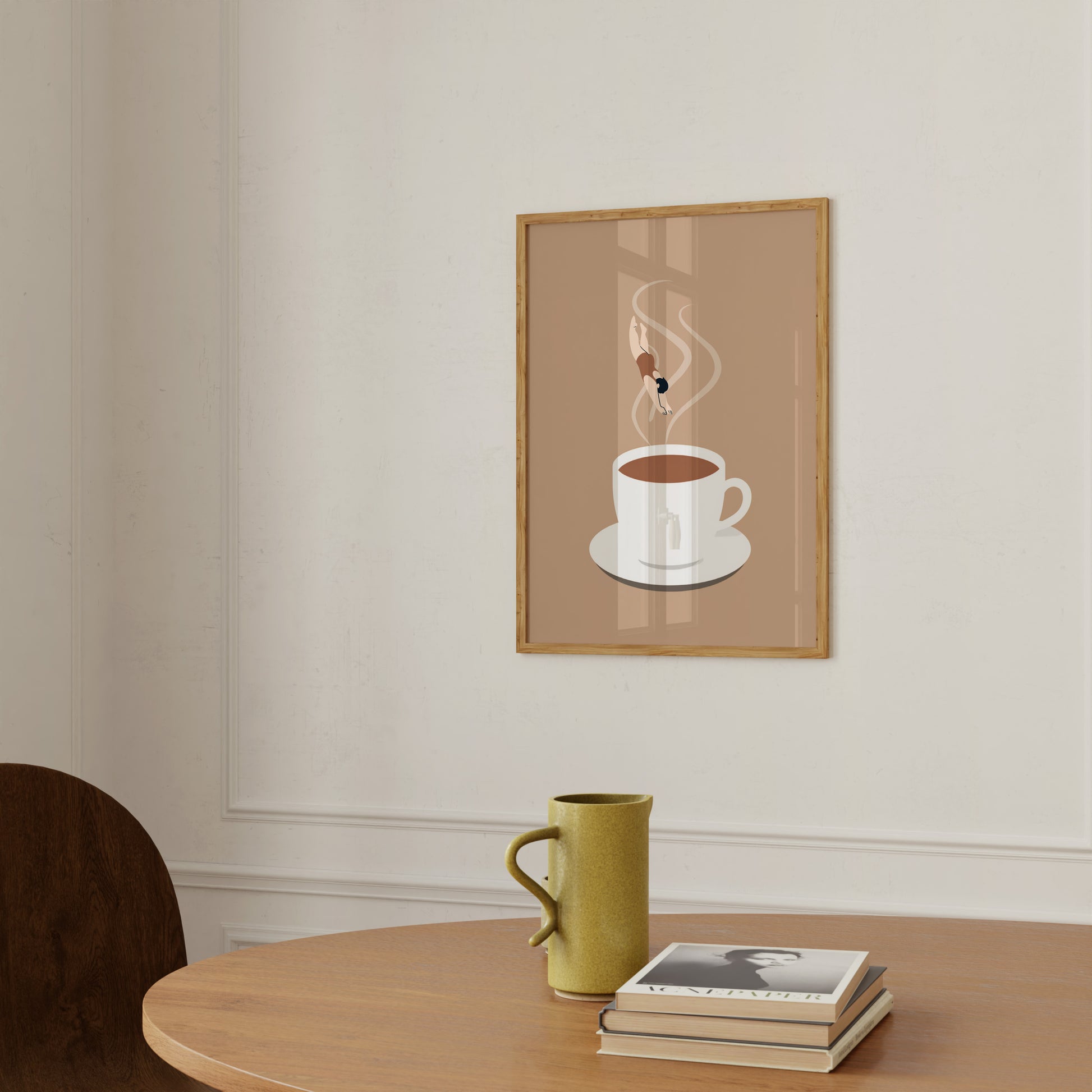 A framed poster of a coffee cup above a mug and book on a wooden table.