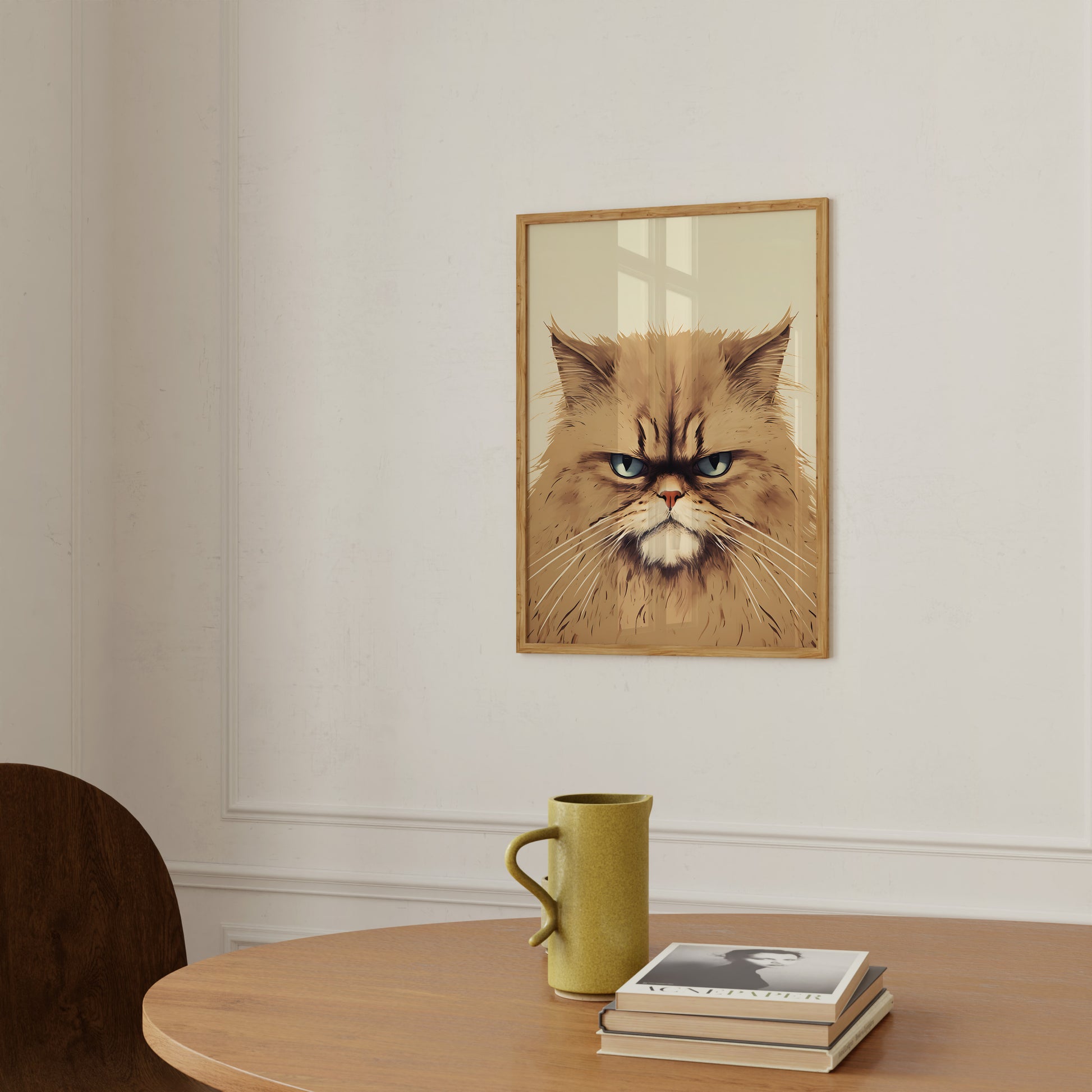 A framed picture of an angry-looking cat on a wall above a table with a mug and books.