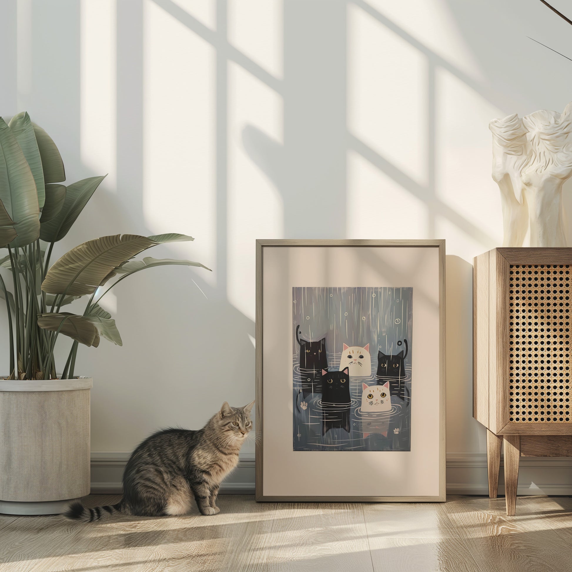 A cat sitting beside a framed picture on the floor in a sunny room with plants and decor.