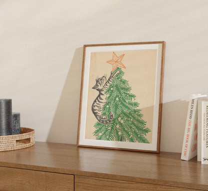 A framed drawing of a cat climbing a Christmas tree placed on a wooden shelf.