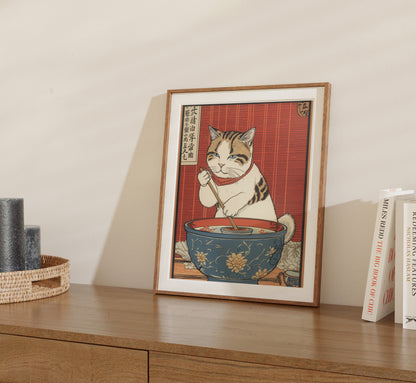 A framed illustration of a cat eating with chopsticks, displayed on a shelf.