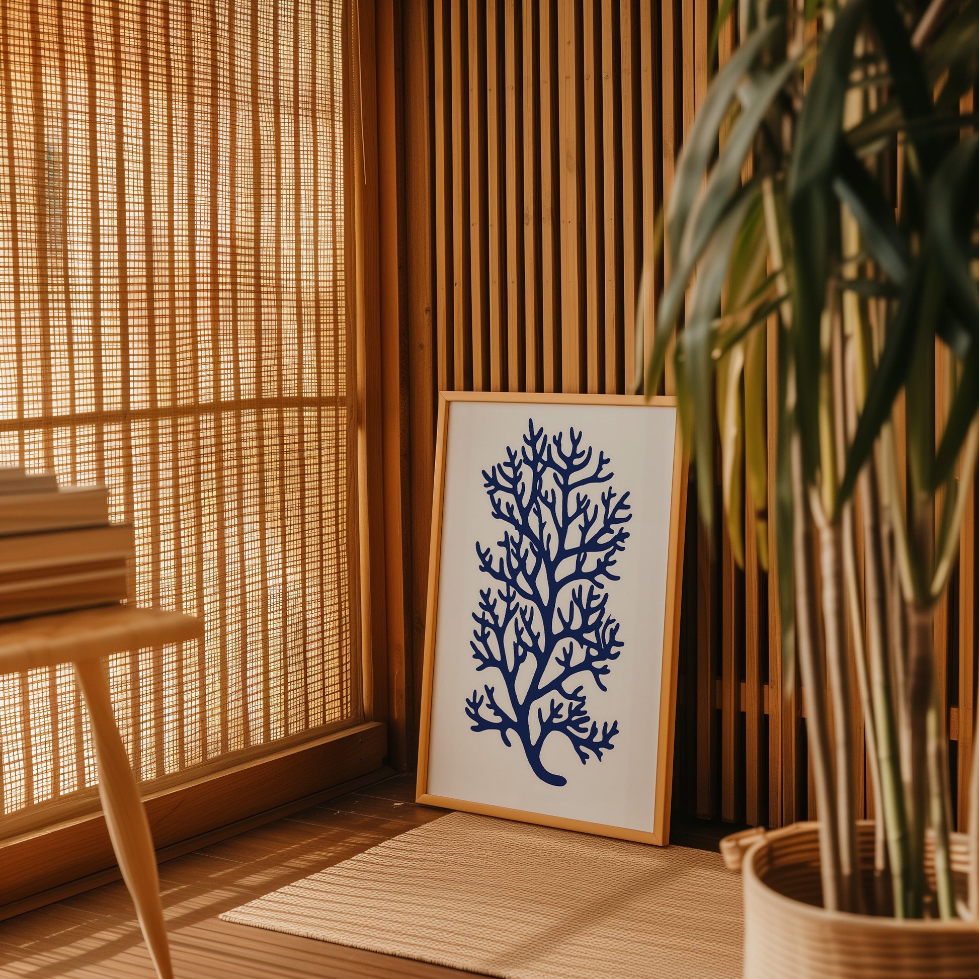 A framed picture of a blue coral on the floor next to a potted plant, with bamboo shades in the background.