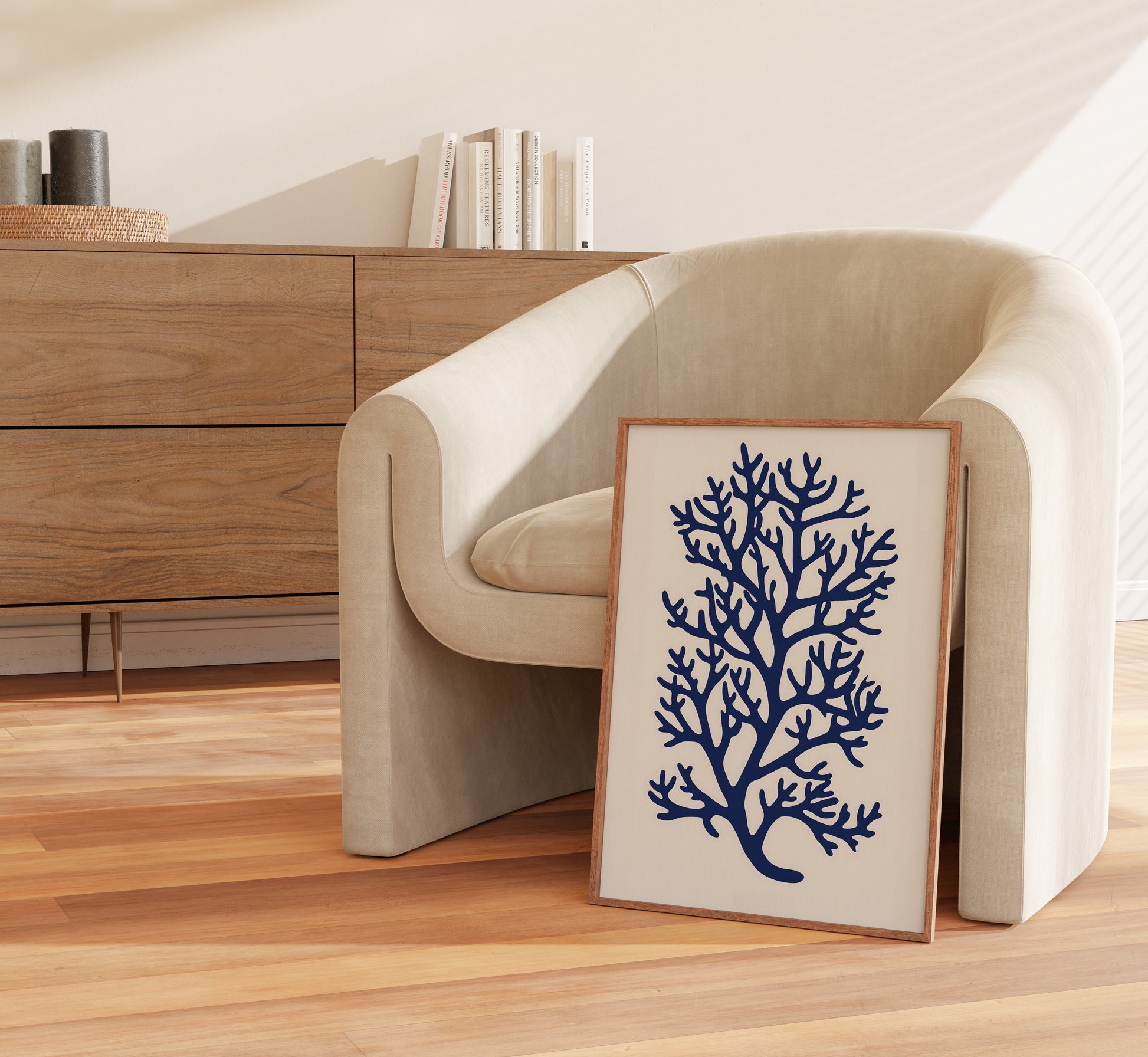 A cozy armchair beside a wooden sideboard with a framed coral illustration leaning against the wall.