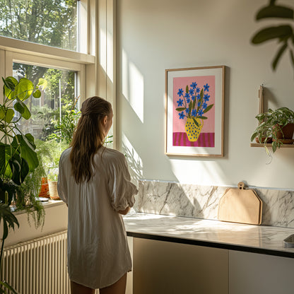 A person stands in a sunny kitchen, looking at a colorful framed artwork on the wall.