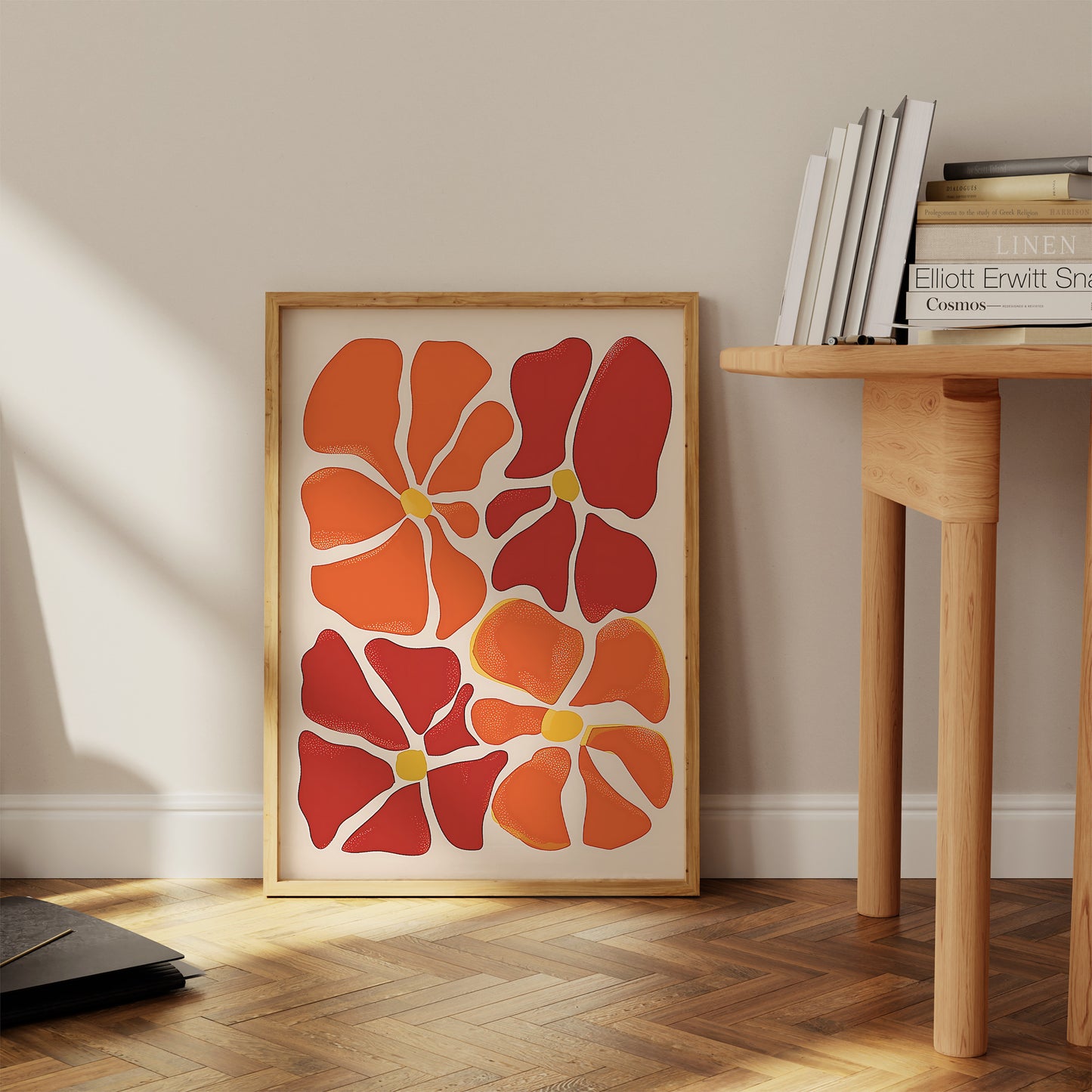 A framed abstract artwork with red and orange shapes beside a wooden table with books.