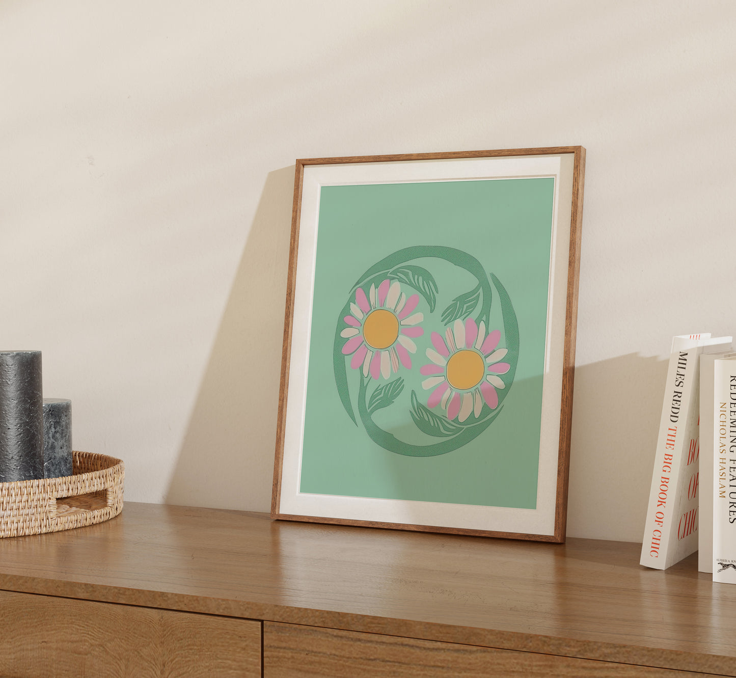 Framed floral print on a desk next to books and a basket.