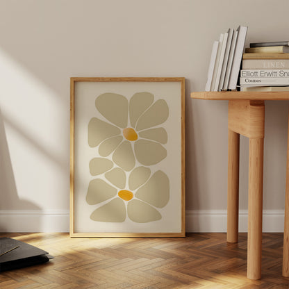 A framed abstract floral print leaning against a wall beside a wooden side table with books.