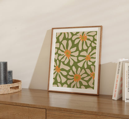 A framed floral print on a wooden sideboard next to books and a small woven basket.